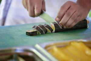 Person schneidet Sushi auf einem grünen Schneidebrett im Hotel Summer Island Maldives.