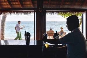 Mitarbeiter serviert Getränke an der Bar im Summer Island Maldives Hotel mit Blick auf den Strand und das Meer.