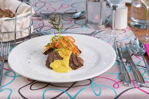 Ein Teller mit Steak, gelbem Soßen und Gemüse auf dem Tisch im Turquoise Hotel.