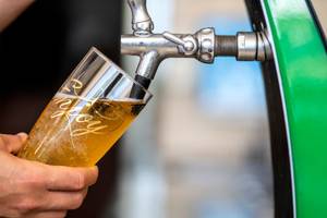 Bier wird aus einem Zapfhahn in ein Glas gezapft, das in der Hand gehalten wird.