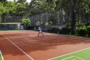 Zwei Spieler spielen Tennis auf einem roten Tennisplatz im Turquoise Hotel.