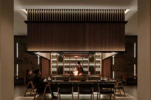 Das Interieur des JAZ Riviera Restaurants mit einem Koch am offenen Feuer, umgeben von Gästen an einem langen Tisch.