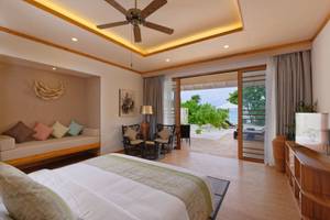 Schlafzimmer im Brennia Kottefaru Maldives mit Bett, Sofa, Fenstern und Blick auf das Meer.