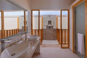 Innenansicht eines Badezimmers im Brennia Kottefaru Maldives Hotel mit zwei Waschbecken und einer Duschkabine.