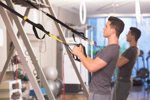 Mann im Fitness-Studio arbeitet mit Fitness-Bands an einer Stange