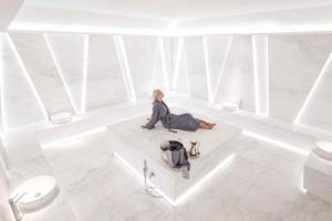 Eine ältere Frau sitzt entspannt in einem weißen Marmor-Spa-Raum des Nikki Beach Resort & Spa Dubai.
