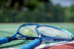 Tennisschläger auf einem Tennisplatz mit einem Tennisball im Hintergrund.