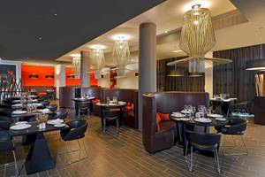 Innenansicht eines modernen Hotelrestaurants mit dunklen Möbeln und großen Leuchten.
