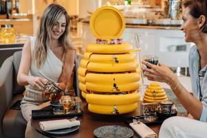 Zwei Frauen genießen Tee am Tisch im Hilton Dubai Palm Jumeirah mit einer gelben Honigwabe.