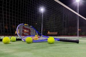 Tennisplatz mit Schläger und Bällen bei Nachtbeleuchtung