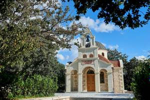 Kleine Kirche mit Glocke und Kuppel umgeben von Bäumen und Sträuchern