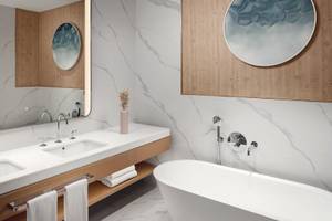 Das Badezimmer im St. Regis Al Mouj Muscat Resort mit Marmorwänden, zwei Waschbecken und einer Badewanne.