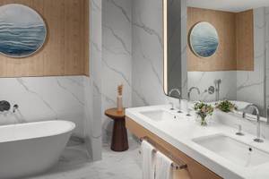 Modernes Badezimmer im St. Regis Al Mouj Muscat Resort mit Badewanne, zwei Waschbecken und Marmorwänden.