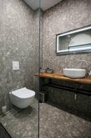 Badezimmer des Oricon Coast Luxury Resort mit grauen Wänden und Bodenfliesen, einer Dusche, einem Waschbecken und einem Toilettensitz.