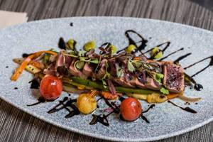 Gegrilltes Lachsfilet auf einem Teller mit verschiedenen Gemüsesorten und einer Soße im Leonardo Royal Hotel Barcelona Fira.