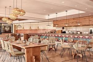 Innenansicht des Restaurants im Atlantica Caldera Palace Hotel mit Holztischen, Rattanstühlen und dekorativen Wandmustern.