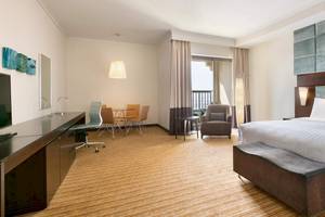 Hotelzimmer im Traders Hotel Qaryat Al Beri mit Schreibtisch, Stühlen, Tisch, Fernseher und Bett.