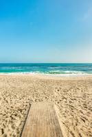 Ein Holzsteg auf einem Strand mit blauem Himmel und klarem Meer.
