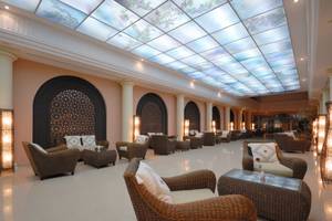Die Lobby des Paradis Palace Hotels mit einem beleuchteten Glasdach und Rattanmöbeln.