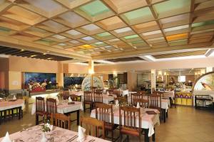 Innenansicht des Restaurants im Paradis Palace Hotel mit gedeckten Tischen, Holzmöbeln und beleuchteter Decke.