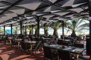 Restaurant im Paradis Palace Hotel mit Tischen und Stühlen unter einer Pergola mit Blick auf den Strand