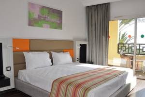 Hotelzimmer im Paradis Palace mit Bett, Kopfteil, Lampe, Gemälde und Balkonzugang.