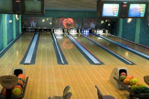 Bowlinghalle mit Bowlingbahnen und Monitoren, die verschiedene Spiele anzeigen.