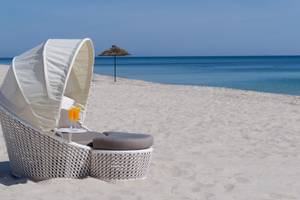 Ein weißer Lounge-Stuhl mit Sonnenschirm auf einem weißen Sandstrand mit Blick auf das blaue Meer.