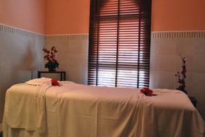 Massage-Behandlungsraum im JAZ Tour Khalef mit einem Massagetisch, weißen Laken, roten Rosen und geschlossenen Jalousien.