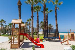 Kinderspielplatz am Strand im JAZ Tour Khalef Hotel mit Palmen und Spielgeräten.