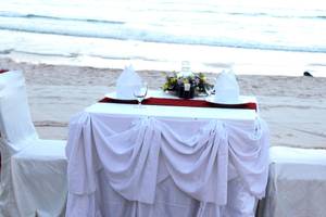 Ein Tisch auf dem Strand mit weißen Tischdecken und Blumen.