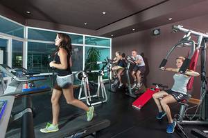 Fitnessstudio im Sahara Beach AquaPark Resort mit mehreren Personen, die auf Laufbändern und anderen Geräten trainieren.