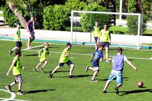 Kinder in neonfarbenen Trikots spielen Fußball auf einem Feld mit einem Tor im Hintergrund.