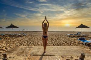 Eine Frau in einem Bikini steht auf einem hölzernen Steg am Strand während des Sonnenuntergangs.
