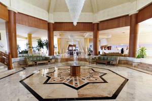 Foyer des Sentido Bellevue Park Hotels mit großen Kronleuchtern, Marmorboden und zentralen Tisch.
