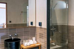 Badezimmer im Banana Fan Sea Resort mit schwarzen Waschbecken, Glasdusche und gefliester Wand.