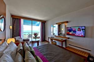 Hotelzimmer mit Meerblick, Fernseher, Bett, Sofa, Tisch und Dekor.