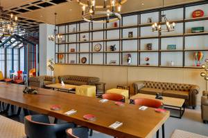 Innenbereich des NH Collection Dubai The Palm Hotels mit langen Holztischen, Stühlen, Couchen und dekorativen Gegenständen an den Wänden.