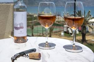 Eine Flasche Wein, zwei Gläser und ein Korkenzieher auf einem Tisch am Strand.