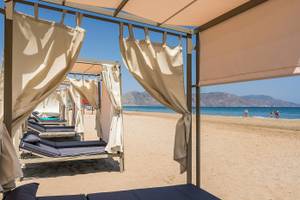 Sonnenliegen am Strand unter Pavillons am Vantaris Palace Hotel