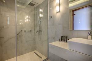 Ein elegantes Badezimmer im Vantaris Palace Hotel mit Marmorwänden, einer Glasdusche und einem Waschbecken.