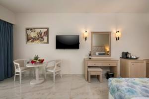 Inneneinrichtung eines Zimmers im Vantaris Palace Hotel mit Tisch, Stühlen, Fernseher, Spiegel und Nachttisch.