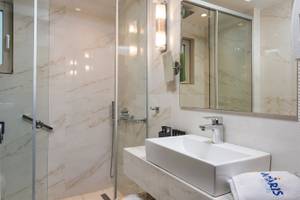 Badezimmer im Vantaris Palace Hotel mit Marmorwänden, Glasdusche und Waschbecken.