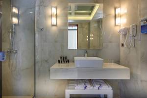 Badezimmer im Vantaris Palace Hotel mit Marmorfliesen, Waschbecken, Spiegel und Föhn.