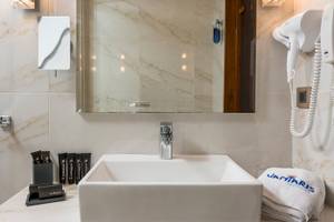 Badezimmer im Vantaris Palace Hotel mit Waschbecken, Spiegel und Handtuchtrockner.