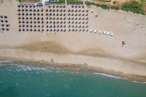 Luftaufnahme des Vantaris Palace Strandes mit vielen Sonnenschirmen und Menschen im Wasser.