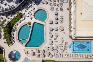 Luftaufnahme des Vantaris Palace Schwimmbadbereichs mit mehreren Pools und Sonnenliegen.