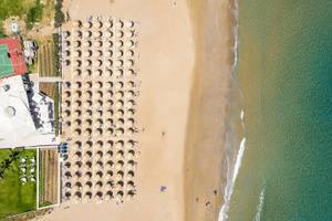 Oberflächenansicht eines Strandes mit vielen Sonnenhüten und einem Hotelgebäude im Hintergrund.