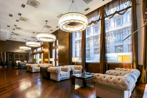 Lobby des Colonial Barcelona Hotels mit weißen Sofas, Holzboden und großen Kronleuchtern.