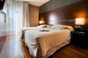 Doppelbettzimmer im Colonial Barcelona Hotel mit Holzboden und gemusterten Wänden.